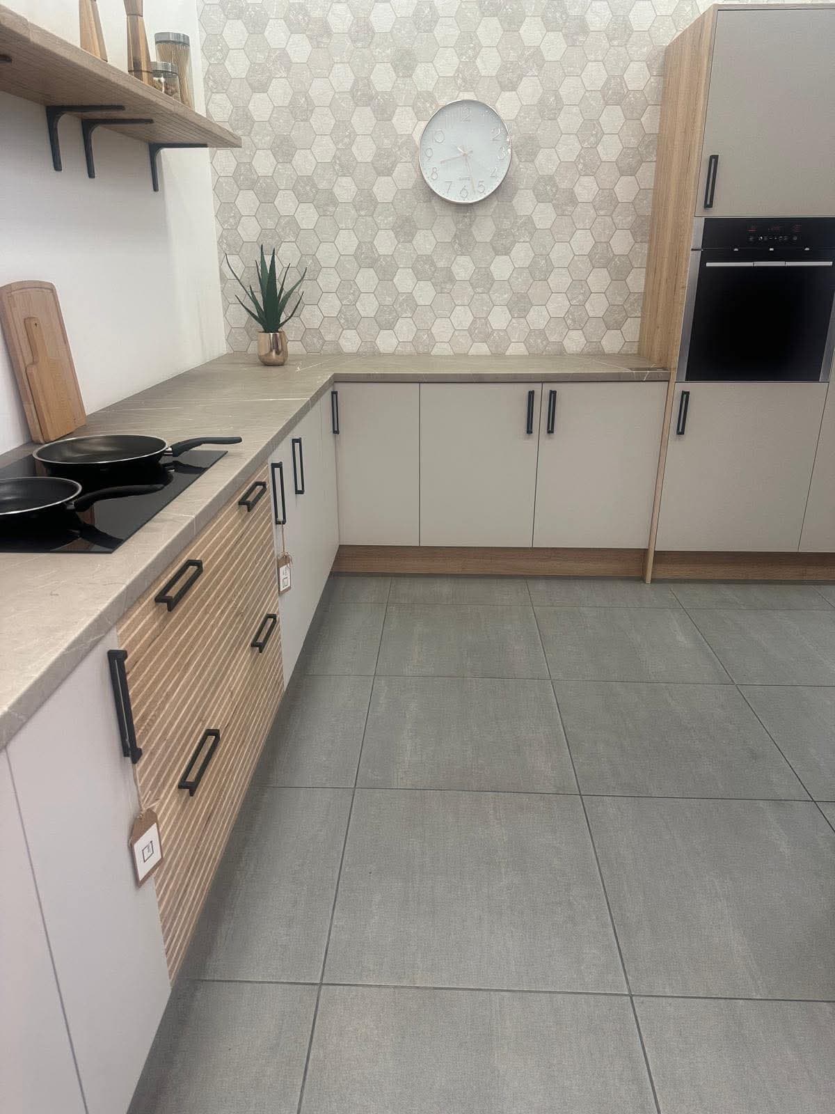 A modern fitted kitchen with cream and wood-tone cabinetry, hexagonal tile backsplash, gray tile flooring, built-in oven, and induction cooktop.