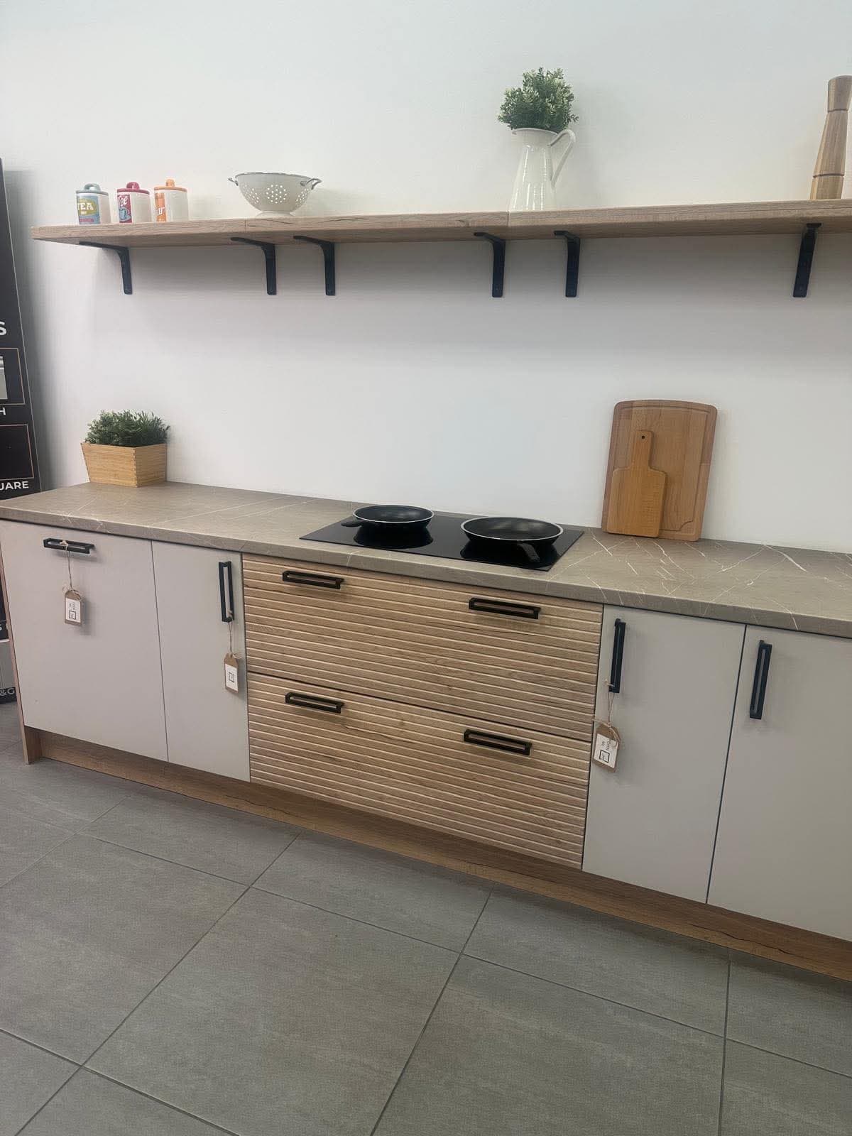 Fitted kitchen with light grey and wood-tone cabinetry, stone worktop, black portable cooktop, floating wooden shelves with black brackets, and matching grey floor tiles.