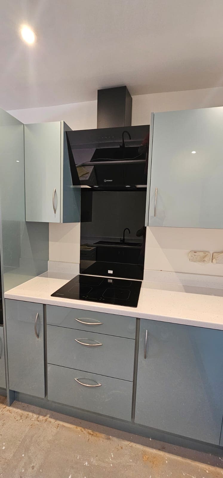 Installed modern kitchen with white and grey cabinetry, white quartz countertop, black induction hob, and black angled range hood with integrated glass splashback.