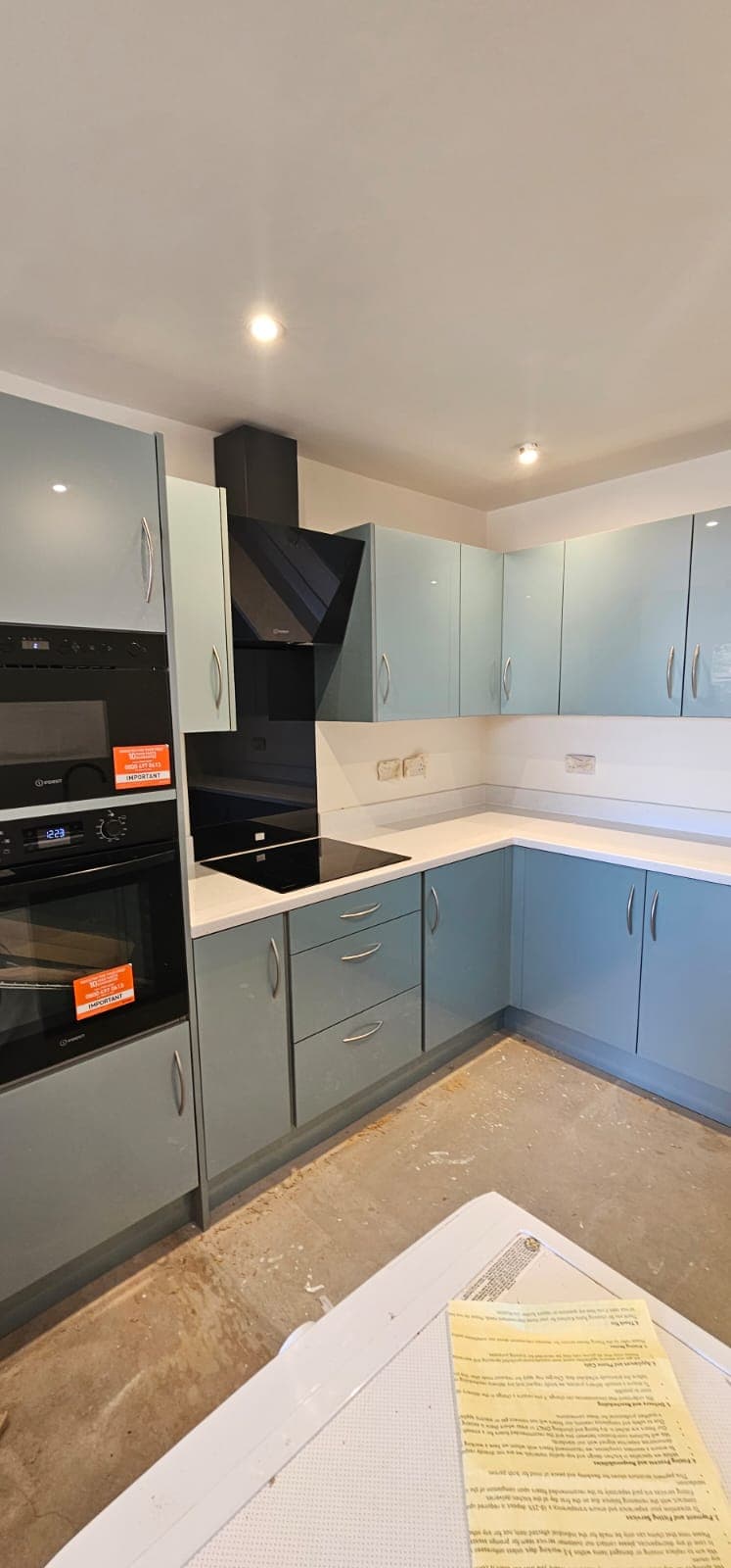 Installed modern kitchen with light blue and white cabinetry, white countertops, black cooktop and dual ovens, and white ceiling with recessed lighting.