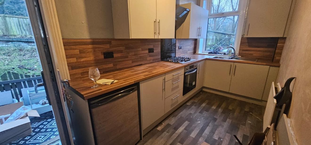 Cream modern kitchen with walnut worktop and brick backsplash, dark integrated oven, gas hob, open garden view with patio.