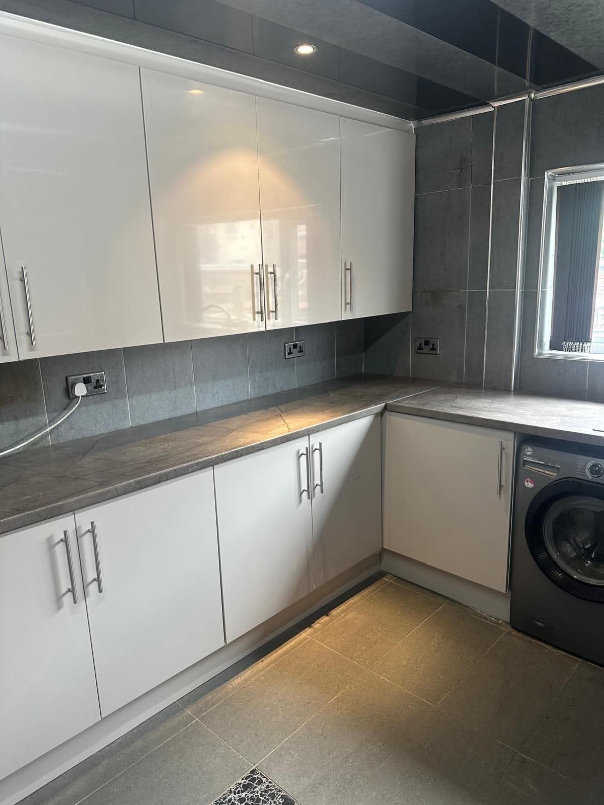 White gloss cabinetry with dark grey tiled backsplash and dark grey stone worktop in a U-shaped layout with integrated washing machine.