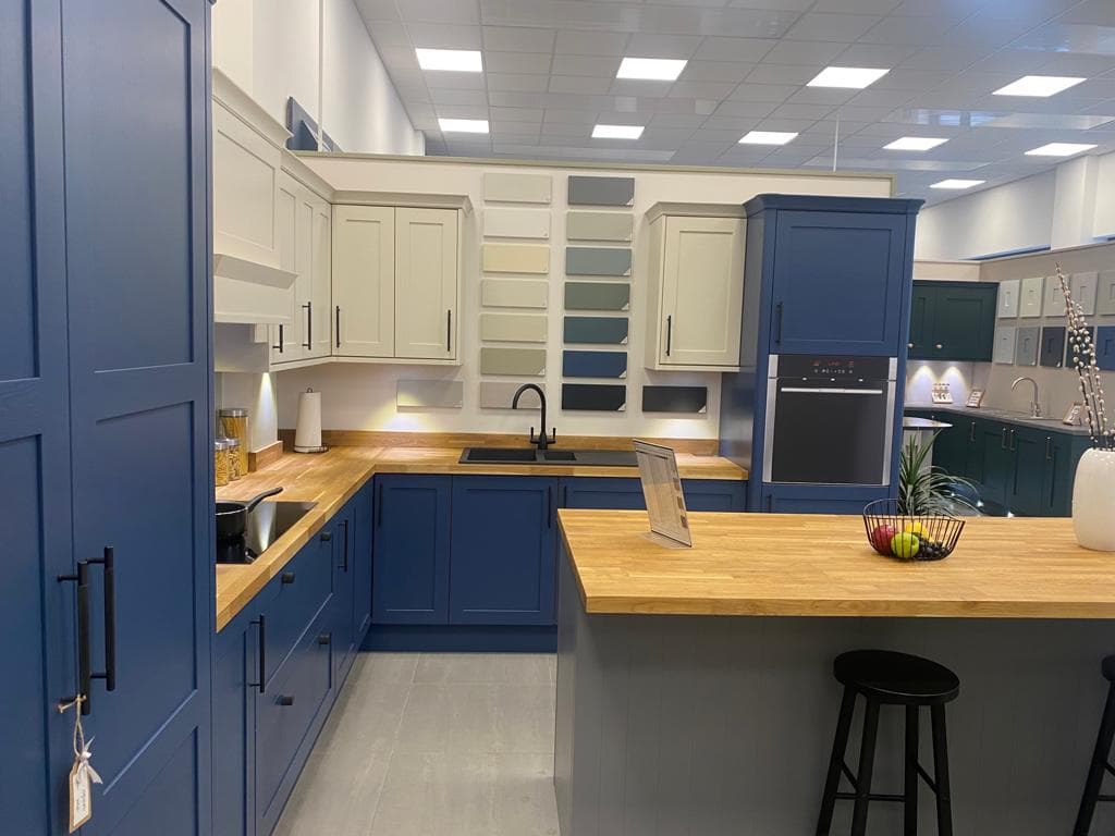 Modern kitchen with navy blue and cream two-tone cabinetry, wood worktops, and an island with seating in a showroom setting.