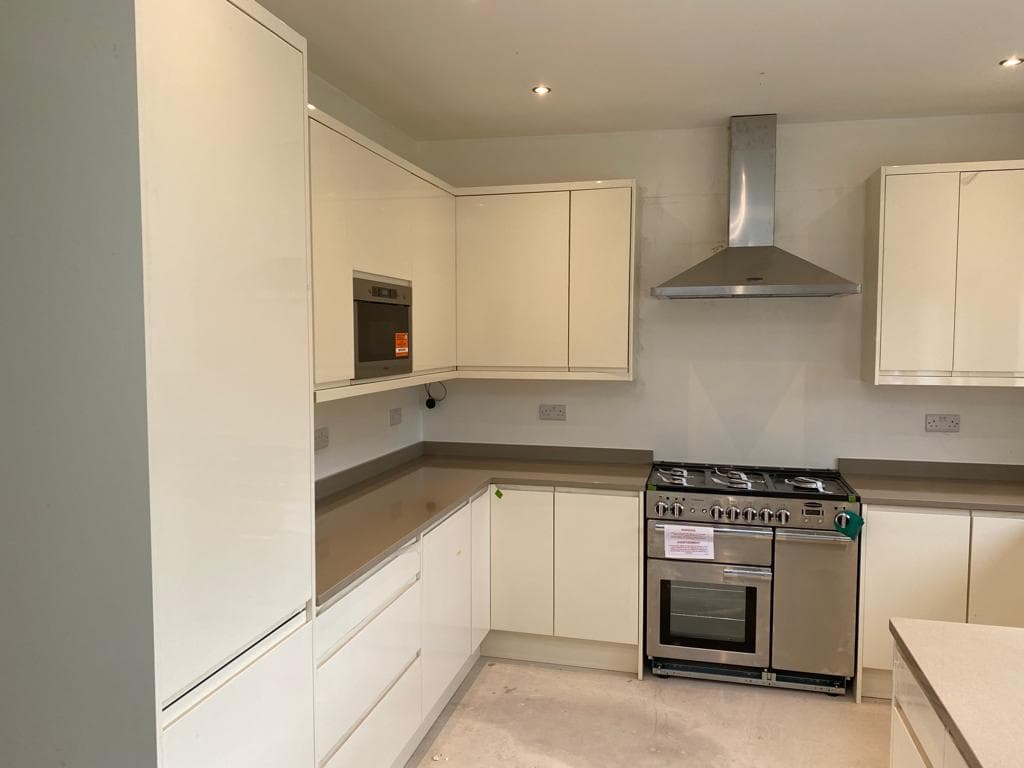 A modern cream and white L-shaped kitchen with integrated appliances, a stainless steel range cooker, and grey stone worktops throughout.