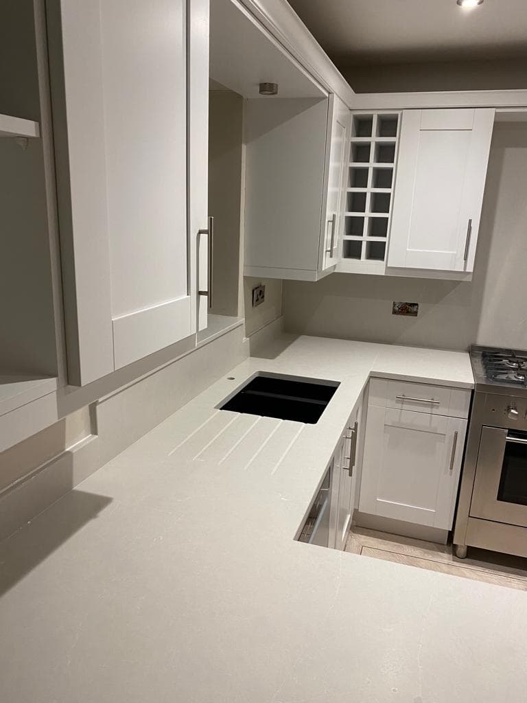 Modern galley kitchen with white painted cabinets, white quartz worktops, stainless steel appliances, and glass-fronted upper cabinets, photographed from above.
