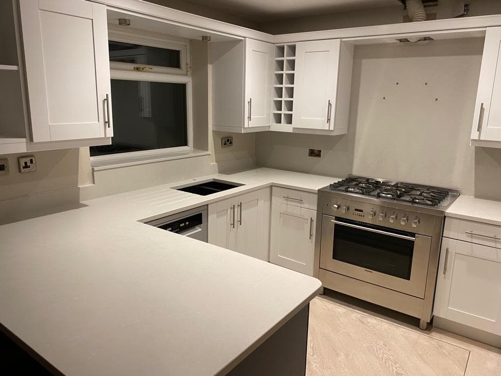 White shaker-style kitchen with cream quartz worktops, stainless steel range cooker, and u-shaped layout with integrated appliances.