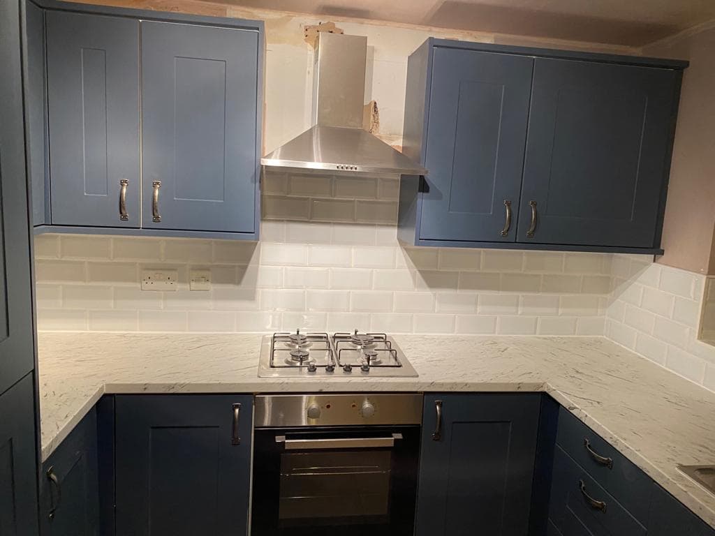 Two-tone shaker kitchen with dark navy lower cabinets, light blue-grey upper cabinets, white metro tile splashback, marble-effect worktops, and stainless steel range cooker with extractor hood in a U-shaped layout.