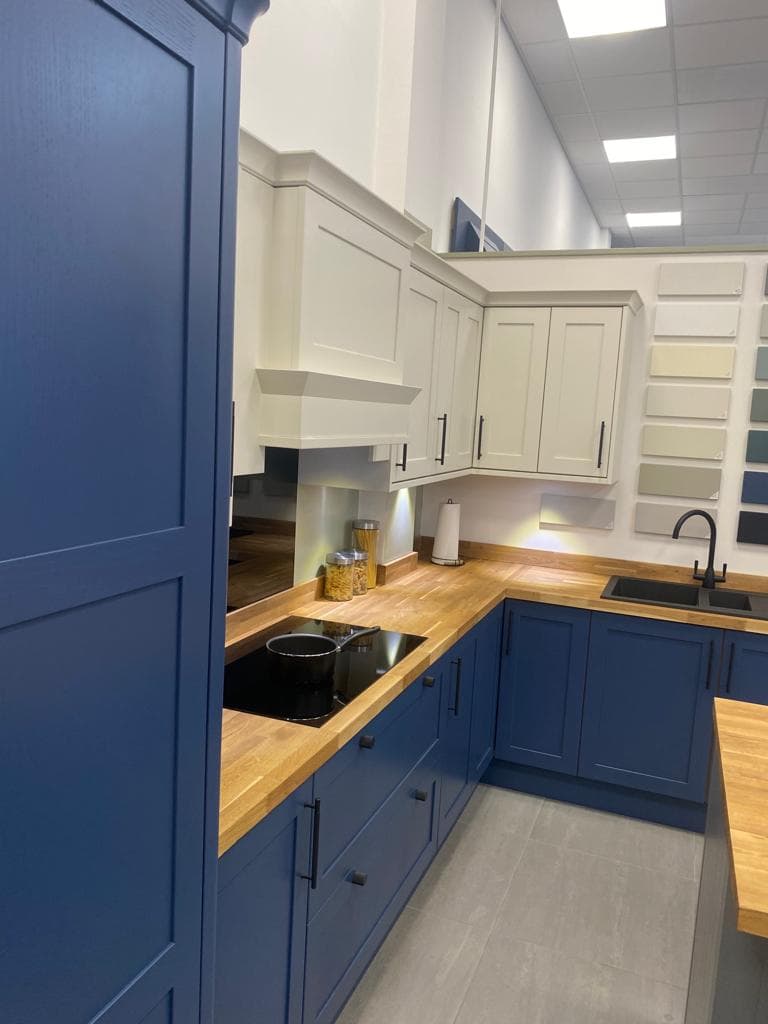 A galley kitchen with navy blue lower cabinets and cream upper cabinets, featuring wooden worktops and a two-tone colour scheme.