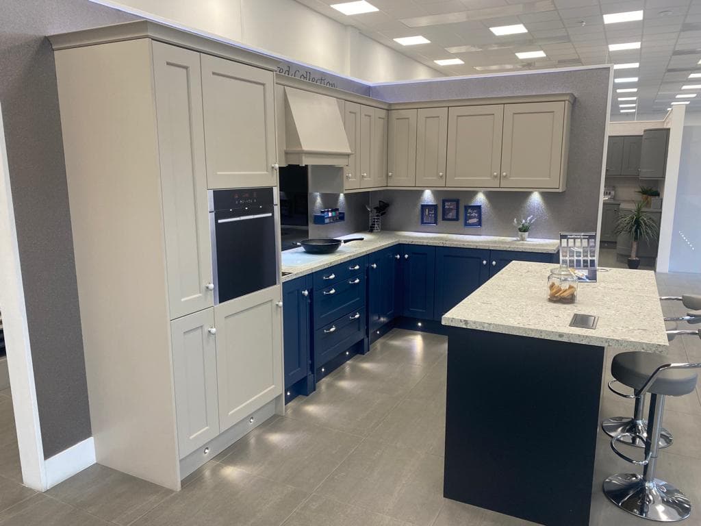 Two-tone shaker kitchen with cream upper cabinets and navy lower cabinets, featuring a large island with stone worktop and integrated seating, stainless steel appliances, and pendant lighting.