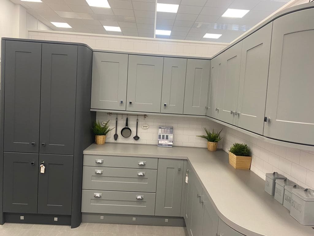 Two-tone shaker kitchen with dark grey and cream painted cabinetry, white subway tile splashback, and light stone worktops in a showroom display.